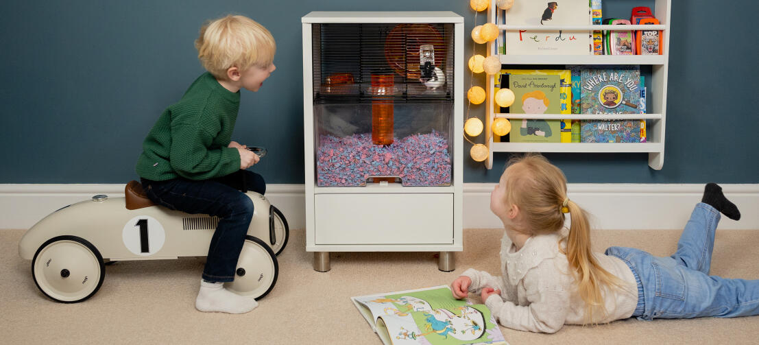 Two children relaxing and playing around the Qute hamster cage in their bedroom.