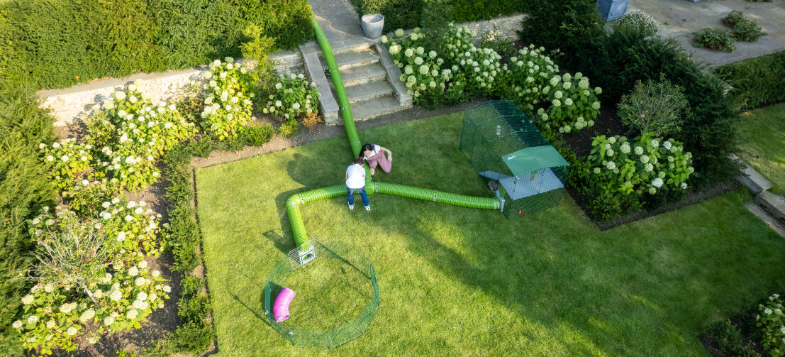 Overhead drone shot of children playing with Zippi tunnel system, attached to playpen and run.