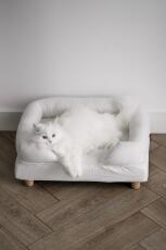 A white cat enjoying the comfort of his white bolster bed