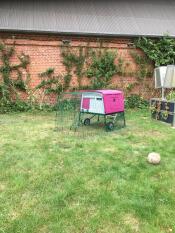 A purple large Eglu Cube chicken coop with a run attached in a garden