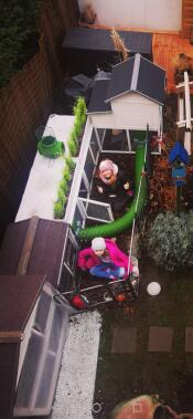Two girls sat in a garden with a Zippi tunnel setup with a rabbit hutch