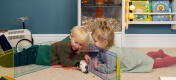 Little boy and girl lying down watching their hamster on the floor.