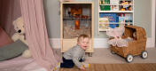 Baby on the floor of a playroom with a Qute hamster and gerbil cage.