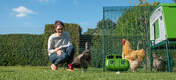 A woman in her back garden with chickens inside a run with a large green Cube chicken coop