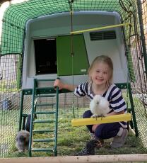 A girl sitting inside an Eglu chicken coop.