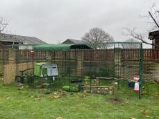 A green chicken coop in a large walk-in run
