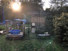 A large outdoor walk in run with a wooden chicken coop inside