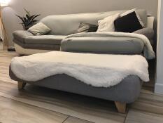 A grey bed with a sheepskin white topper and square wooden feet