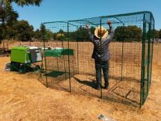 Man setting up Omlet walk in chicken run with Omlet green Eglu Cube large chicken coop and run