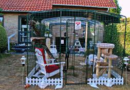 A large walk in run set up for cats with lots of toys and accessories in a garden