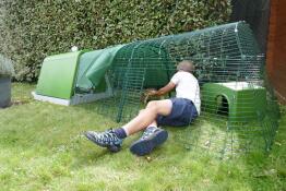 A person demonstrating how to clean a rabbit run connected to a green hutch