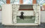 A small black dog on a green bolster bed inside a Fido Studio with a wardrobe attached and curtains in front